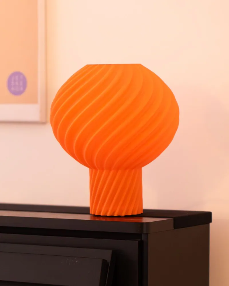 Oranje Helio Lamp op een zwarte piano bij daglicht