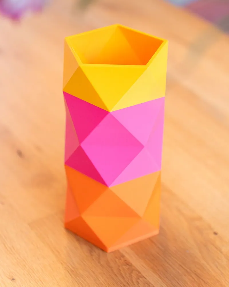 Kami Vase in geel, roze en oranje kleurvlakken op een houten tafel